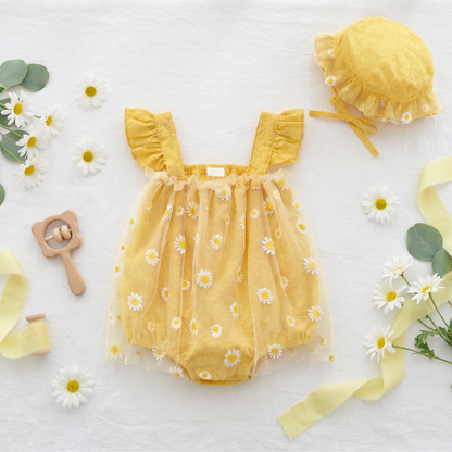 Yellow baby romper with daisy pattern and matching hat on a white background with flowers and a rattle.